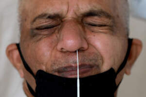 A man wearing a protective face mask reacts as a doctor takes a swab from his nose to test for the coronavirus.